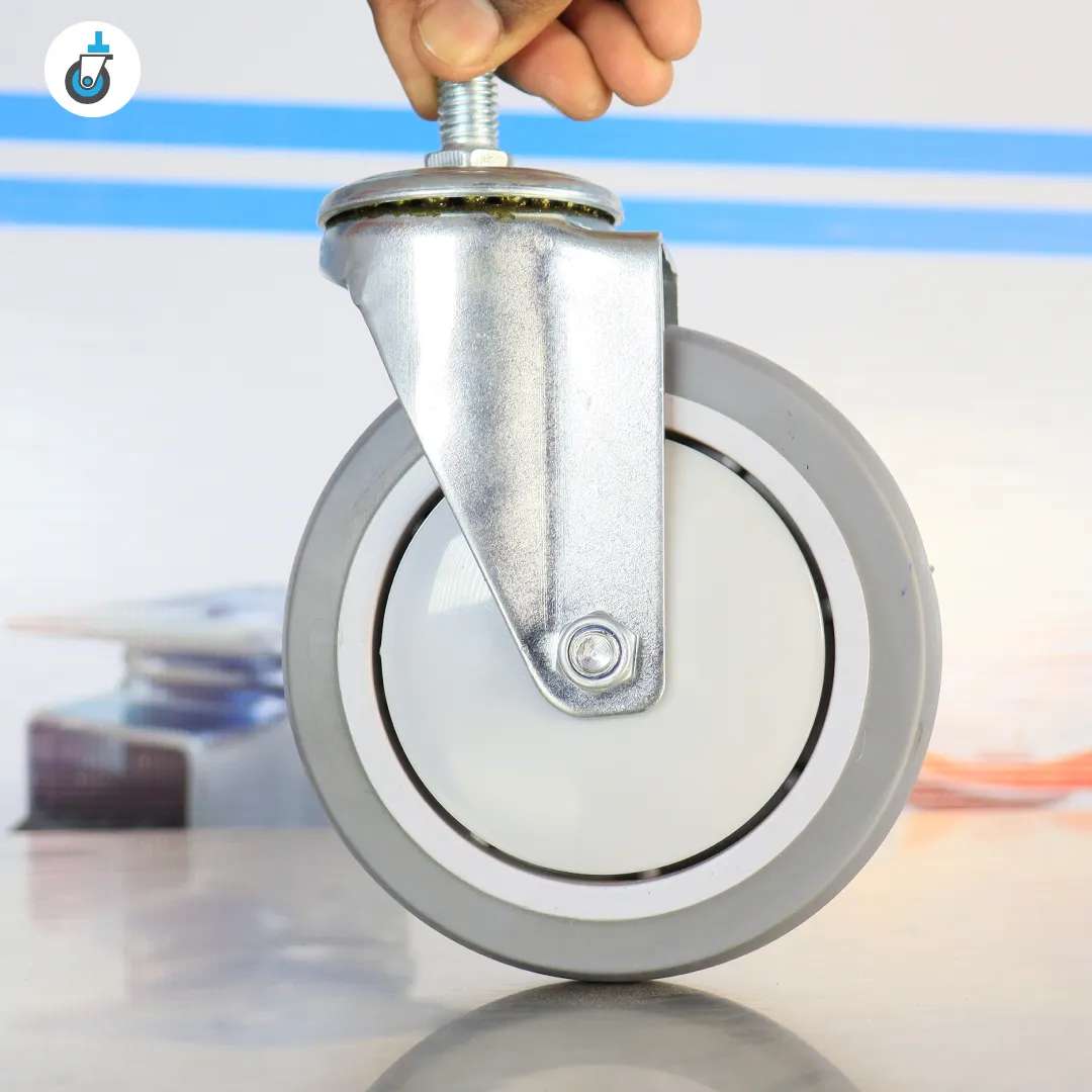 Side view of a 5 inch grey TPR swivel castor with threaded stem held by hand against neutral background.